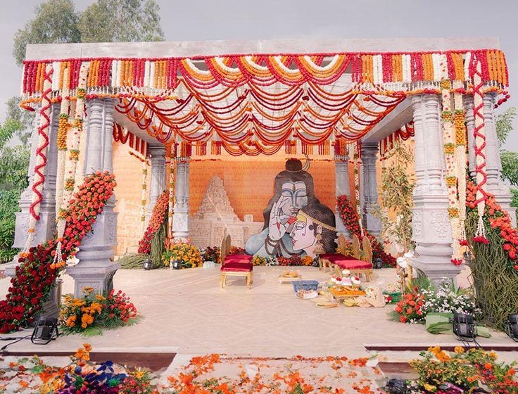 Traditional mandap with stone pillars, a red and white canopy and marigold garlands by RAW Group